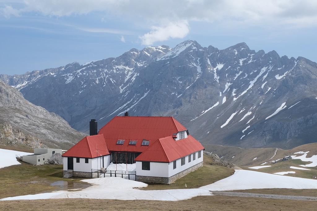 Ein stattliches Haus aus Haupthaus und zwei Nebengebäuden steht vor einer Kulisse aus Bergen