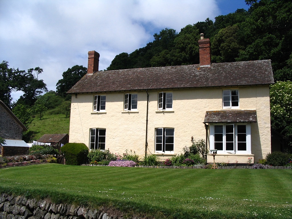 Das Foto zeigt die Selworthy Farm, ein hellgelb gestrichenes Haus mit einem grünen Rasen davor